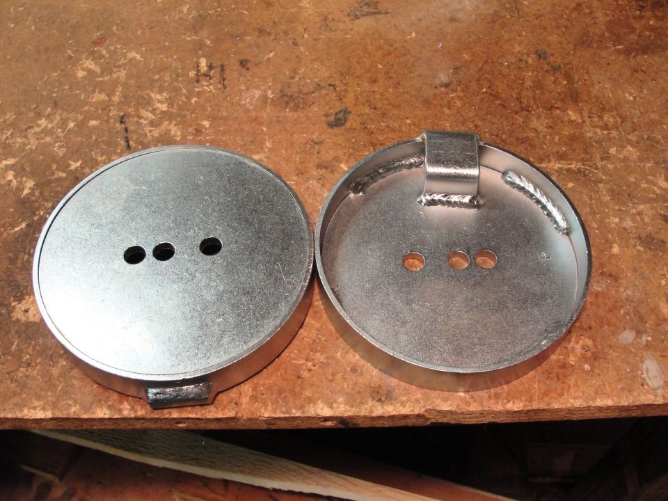 two metal caps with three holes each, one has a welded bracket