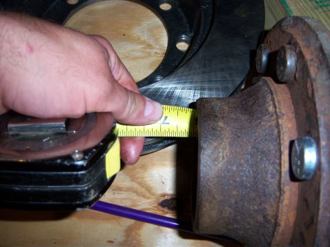 1996 Ford Bronco - A tape measure is used to measure a brake rotor against a rusty hub assembly.