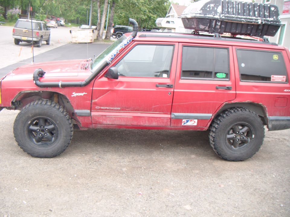 Red Jeep Cherokee with snorkel and roof cargo box. Has 'Sport' and 'Cherokee' badges