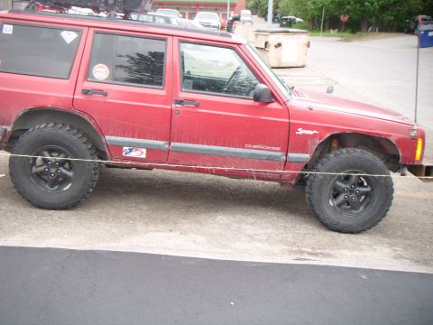 1998 Jeep Cherokee - A red 1998 Jeep Cherokee is viewed from the side, showing its lifted suspension and off-road tires.