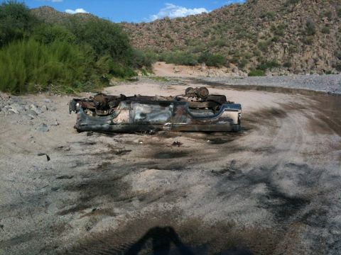1987 Suzuki Samurai - A severely damaged vehicle chassis rests in a dry riverbed under a desert sky.