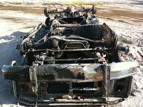 1987 Suzuki Samurai - Chassis of a severely damaged vehicle, likely from a fire, resting on sandy ground.