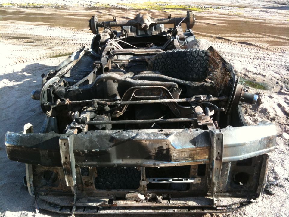 Burnt-out vehicle chassis with front bumper, suspension, and spare tire visible