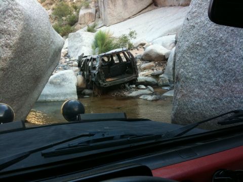 1987 Suzuki Samurai - This burned-out vehicle is submerged in a rocky stream bed, surrounded by large boulders.