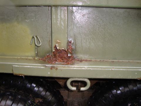 1970 Jeep Commando - Detail of rust damage on a vehicle's lower body panel, near a tow hook and tire.