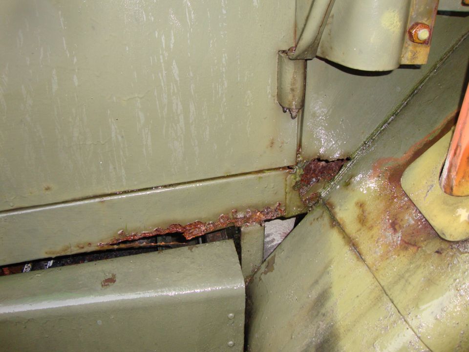 Olive drab metal panel with significant rust damage along the seam and hinge area