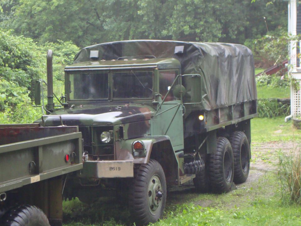 Olive-drab military 6x6 cargo truck with canvas bed cover parked on grass