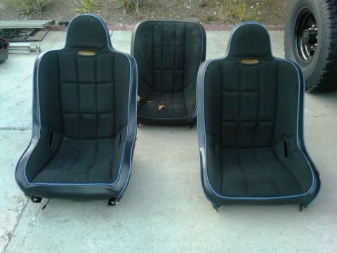 1986 Ford Bronco - Three black bucket car seats with blue piping are laid out on a concrete surface. The middle seat shows signs of wear.