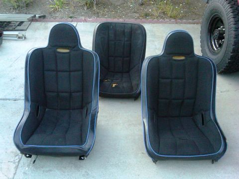1986 Ford Bronco - Three car seats are displayed, two are modern racing seats and one is an older, worn seat. A tire from a vehicle is visible on the right.