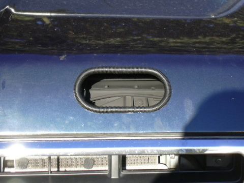 1991 Ford Bronco - Close-up of a dark blue vehicle body panel with an oval opening ringed by black corrugated trim, revealing gray interior components behind…