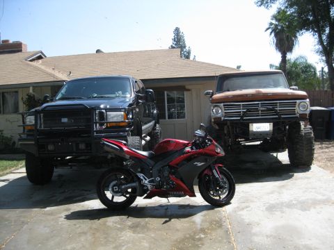 1969 Ford F-250 - A trio of vehicles, including two lifted trucks and a sportbike, are parked in a driveway on a sunny day.