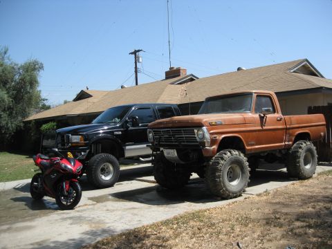 1969 Ford F-250 - An orange pickup truck, a black pickup truck, and a red motorcycle are parked in a driveway on a sunny day.