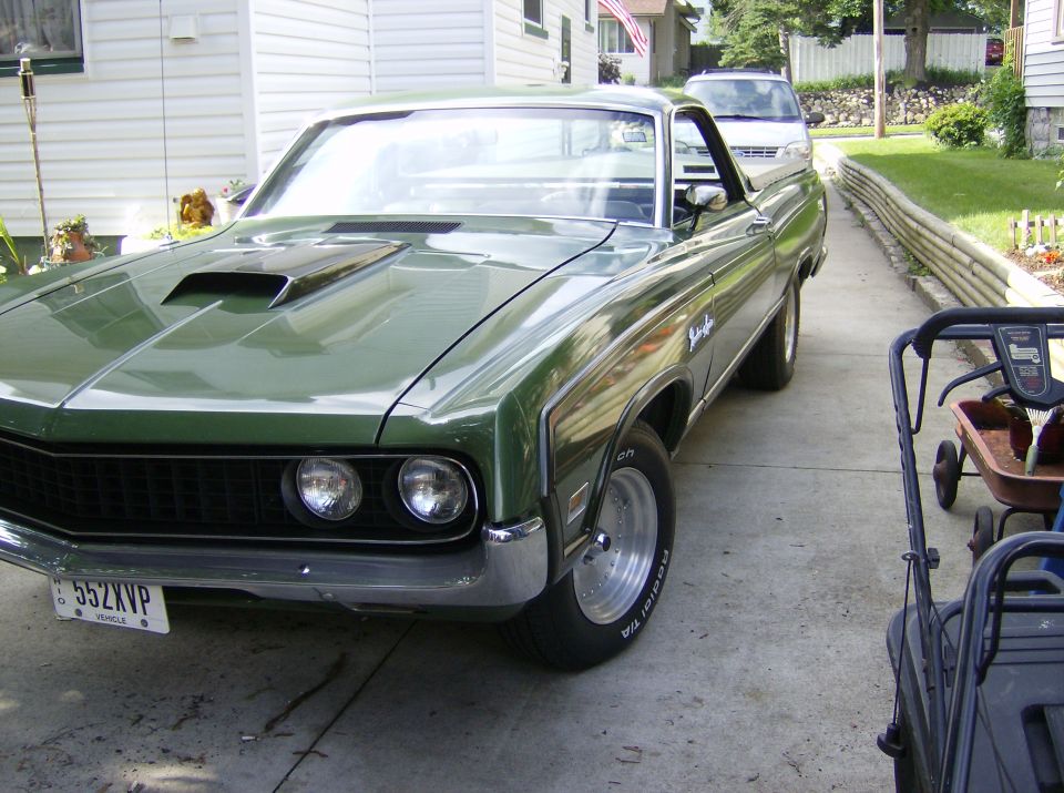 Dark green Ford Ranchero with hood scoop, 3/4 front view on a driveway