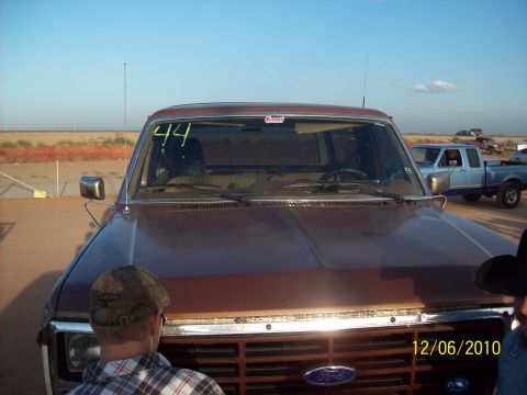 1985 Ford Bronco - A brown 1985 Ford Bronco is seen from the front, with the number 44 written on the windshield. Another blue Ford truck is visible in the ba…