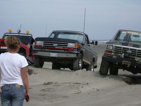 1991 Ford Bronco - Several trucks are parked on a sandy beach, with the ocean visible in the distance.