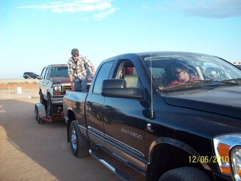 1985 Ford Bronco - A black Dodge Ram 2500 tows a trailer with a Ford Bronco, under a clear blue sky.