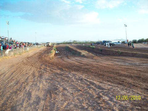 1985 Ford Bronco - Dirt track racing scene with spectators and vehicles under a partly cloudy sky. Date stamp visible.