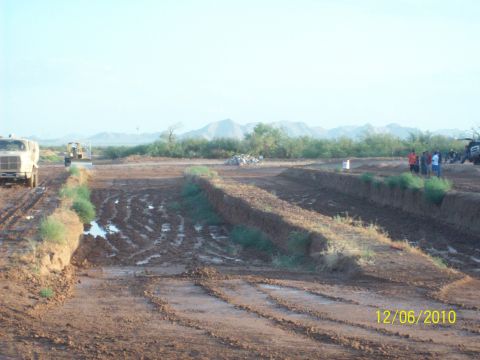 1985 Ford Bronco - A muddy off-road area with construction vehicles and people gathered.