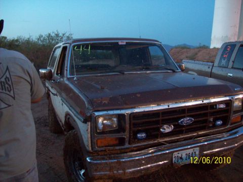 1985 Ford Bronco - A muddy 1985 Ford Bronco is seen from the front, with the number '44' written on its windshield. Another vehicle is visible to the right.