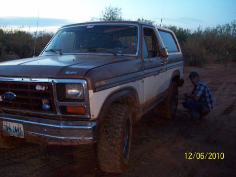 1985 Ford Bronco - 1985 Ford Bronco in outdoor setting with a person attending to the front wheel.