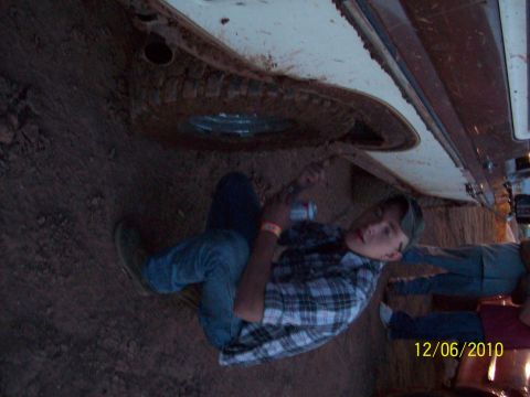 1985 Ford Bronco - A person works on the muddy undercarriage of a vehicle, with the spare tire visible.