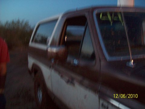 1985 Ford Bronco - A two-tone Ford Bronco is seen from the side in a dusty outdoor setting.
