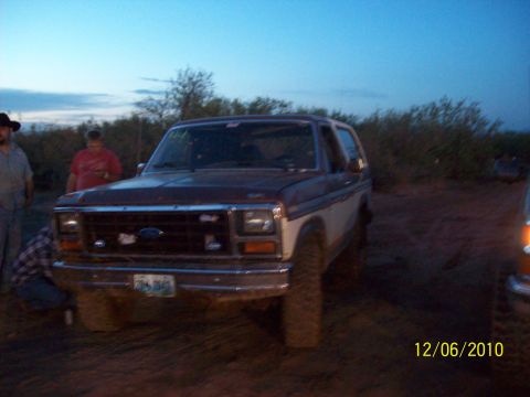 1985 Ford Bronco - A brown and white Ford Bronco is parked outdoors at dusk with people nearby.