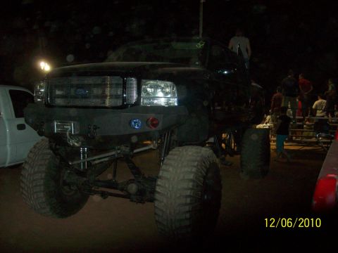 1985 Ford Bronco - A heavily modified black pickup truck is shown at night, with a custom front bumper and large off-road tires.
