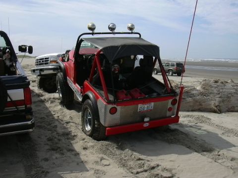 1991 Ford Bronco - Several vehicles are parked on a beach, including a red off-road vehicle and a white Ford truck.