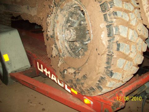 1985 Ford Bronco - A heavily mud-covered tire sits on a U-Haul trailer ramp, obscuring vehicle details.