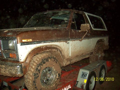 1985 Ford Bronco - This muddy Ford Bronco is loaded onto a trailer, its two-tone paint job barely visible beneath the dirt.