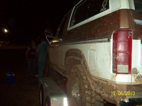 1985 Ford Bronco - This heavily muddied Ford Bronco is seen from the side, loaded onto a trailer at night.