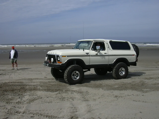 White lifted Ford Bronco with winch and big mud tires parked on a beach by the surf