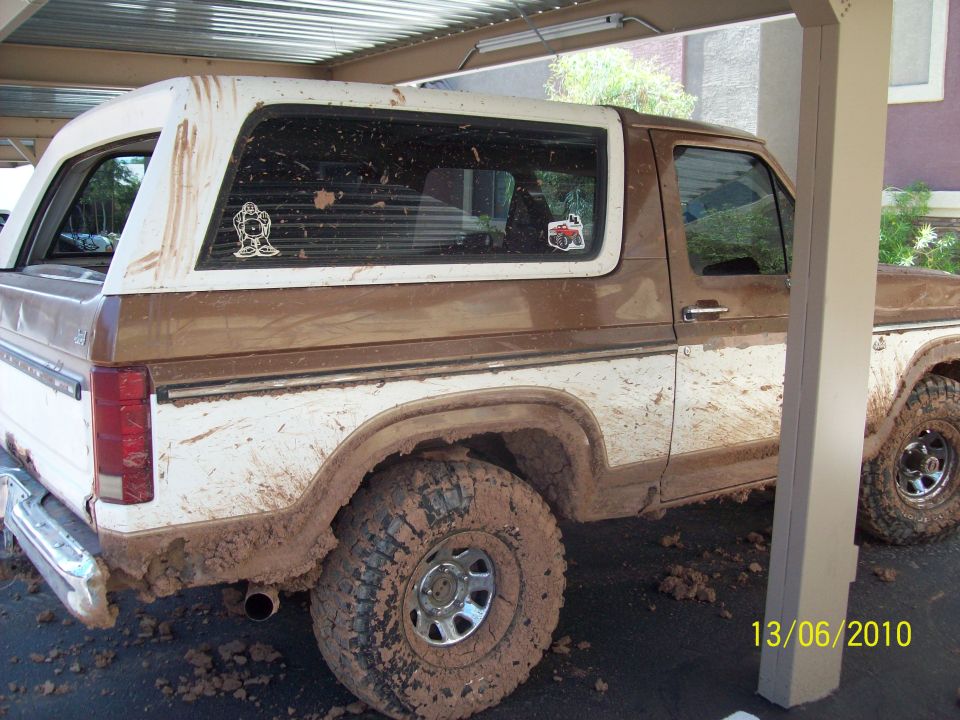 Side view of a mud-covered 1985 Ford Bronco with white removable top