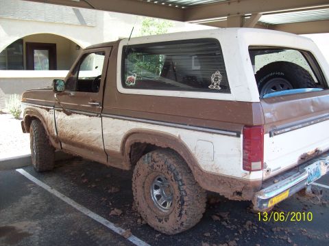 1985 Ford Bronco - This mud-splattered Ford Bronco is parked under a covered area, its tires and lower body covered in dirt.