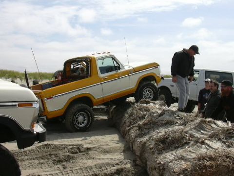 1991 Ford Bronco - Ford Bronco navigating driftwood on the beach, with a white truck in the background.
