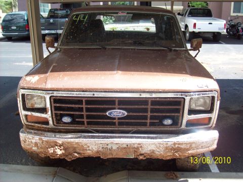 1985 Ford Bronco - This weathered Ford truck, likely from the early 1980s, shows significant rust and mud accumulation on its front end.