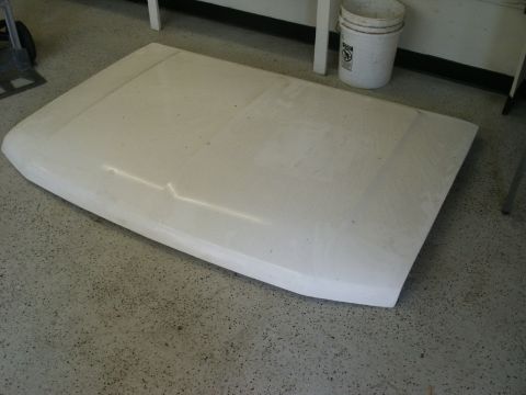 1990 Ford Bronco - A white car hood rests on a concrete floor, with a white bucket and a cart visible in the background.