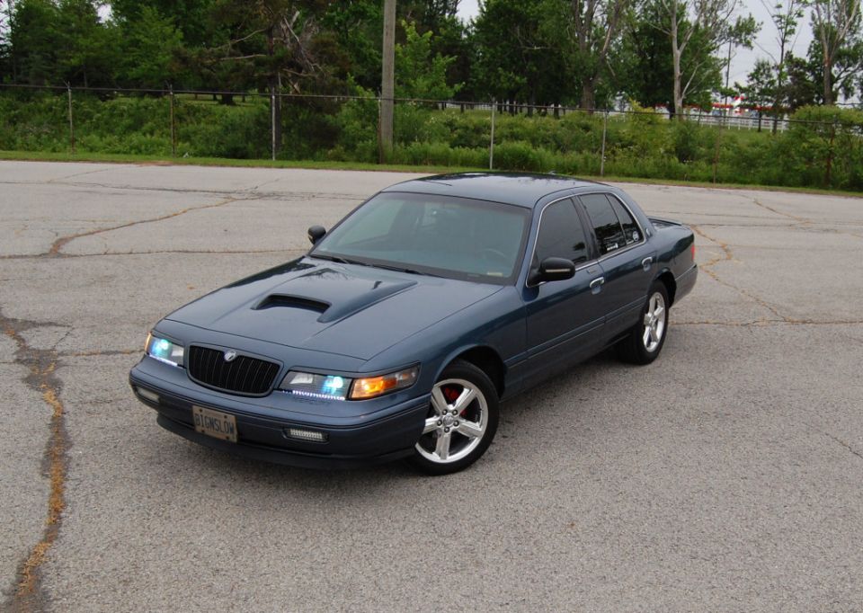 Blue sedan with hood scoop, aftermarket wheels, and custom headlights parked on asphalt