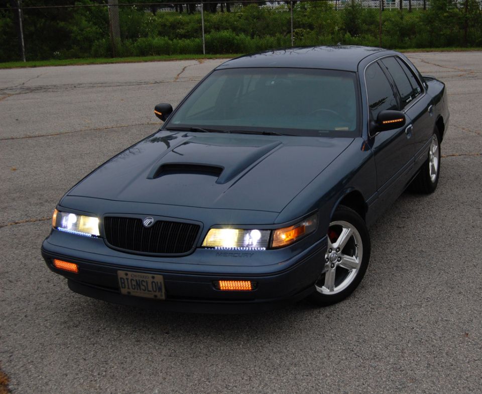 Dark blue sedan with hood scoop and aftermarket wheels, front 3/4 view