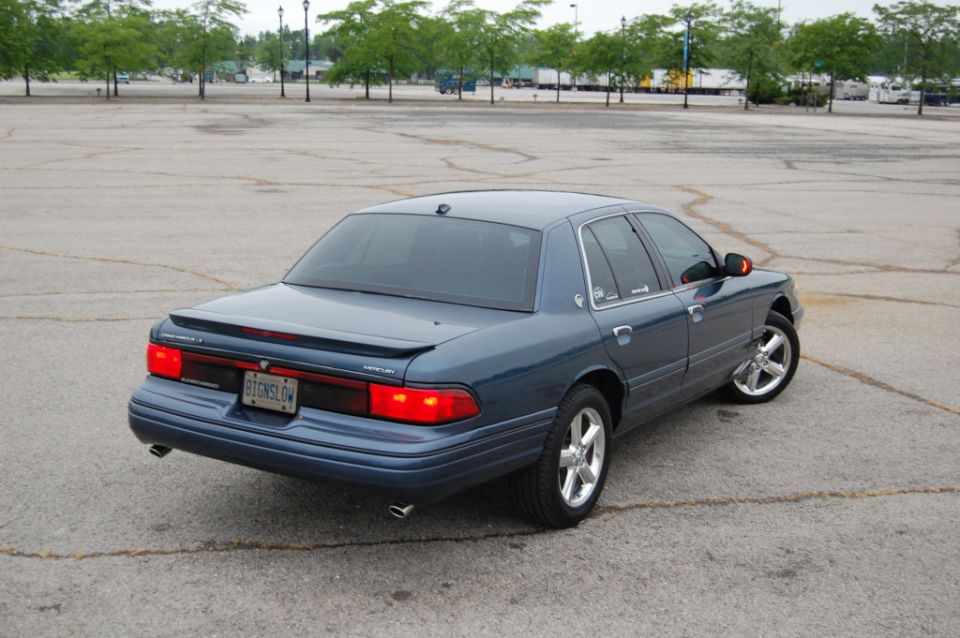 Blue sedan from rear quarter, showing taillights and chrome wheels