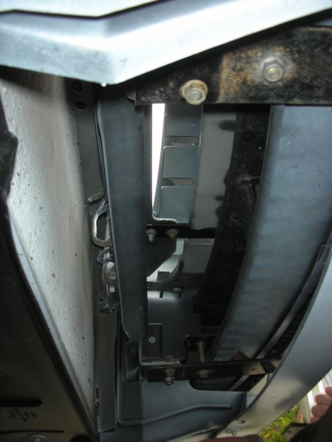 2004 Ford Crown Victoria - Rotated close-up looking down into the front of an engine bay with the grille/bumper cover pulled away, showing the dusty radiator core, bl…