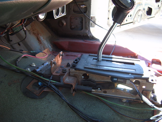 Interior view of a car's automatic transmission shifter and floor console with exposed wiring and rust