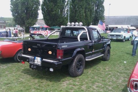 1991 Ford Crown Victoria - Black Jeep Comanche pickup truck parked on grass with other vehicles and tents in the background.