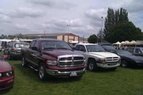 1991 Ford Crown Victoria - A maroon Dodge Ram pickup truck is parked on a grassy field alongside other vehicles under a cloudy sky.