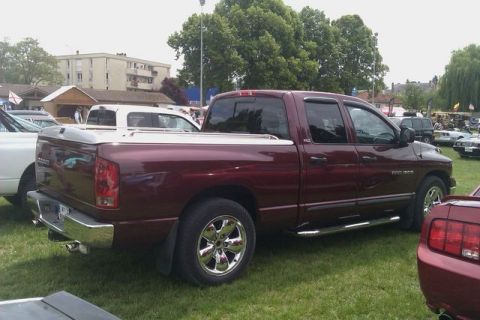 1991 Ford Crown Victoria - A maroon Dodge Ram pickup truck is seen from the rear three-quarter angle, parked on a grassy field with other vehicles present.