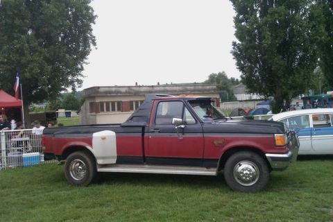 1991 Ford Crown Victoria - A two-tone red and black Ford F-Series truck is parked on a grassy field next to a vintage sedan.