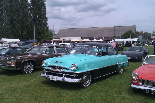 Turquoise and black 1954 Plymouth Belvedere sedan parked on grass with other vehicles