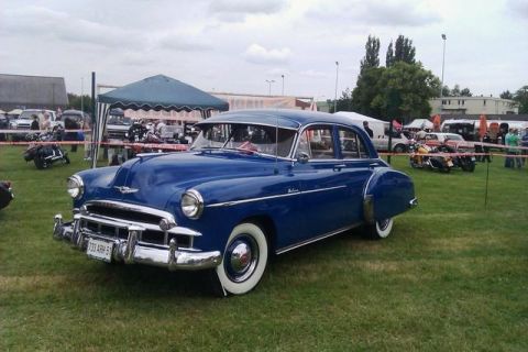 1991 Ford Crown Victoria - A classic blue sedan with whitewall tires is parked on a grassy field at an outdoor event.