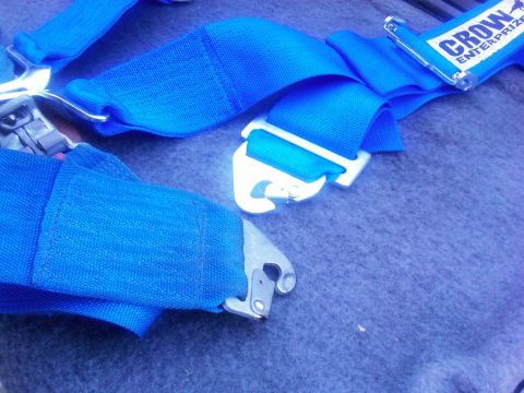 1986 Ford Bronco - Close-up of a blue racing harness, showing the buckle mechanism and a "CROW ENTERPRIZE" label.